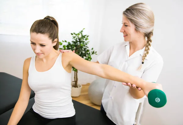 Un fisioterapeuta de rehabilitación moderna en el trabajo con el cliente. Trabajar en hombro con mancuernas — Foto de Stock