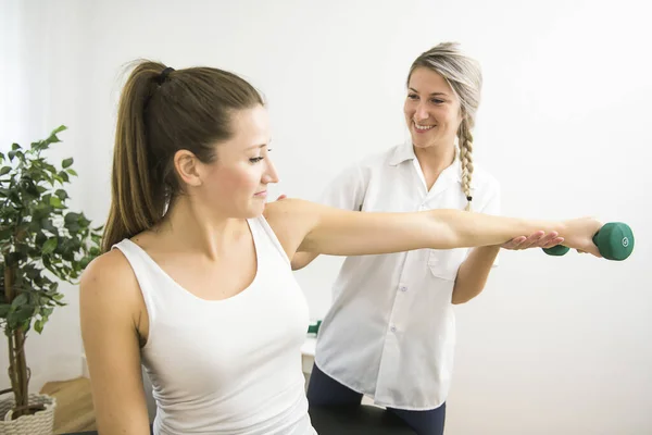 A Modern rehabilitation physiotherapist at work with client. Working on shoulder with dumbell — Stock Photo, Image
