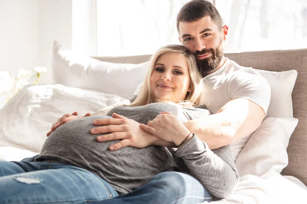 Мужчина прислонился к детской шишке своей беременной жены, которая лежит на кровати — стоковое фото