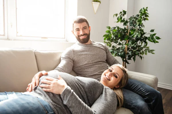 Un uomo che abbraccia una donna incinta felice seduta sul divano — Foto Stock