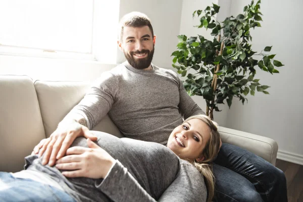 Een man omhelst gelukkige zwangere vrouw zittend op de bank — Stockfoto