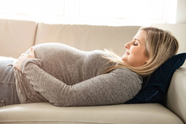 Счастливая беременная женщина, лежащая дома на диване — стоковое фото
