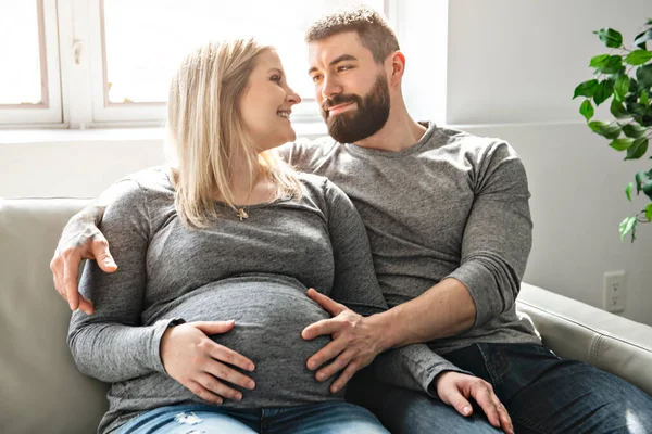 Um homem abraçando mulher grávida feliz sentado no sofá — Fotografia de Stock