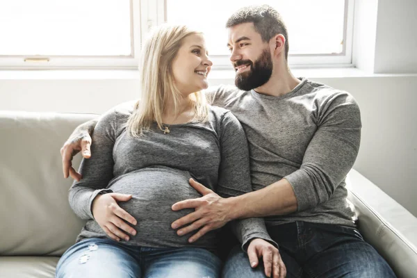 Мужчина, обнимающий счастливую беременную женщину, сидящую на диване — стоковое фото