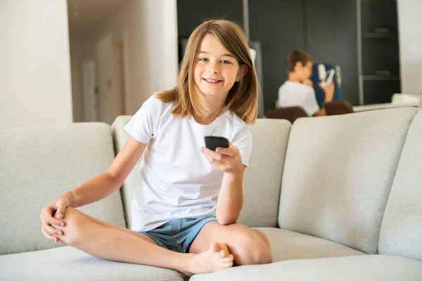 Una chica sosteniendo el control remoto y viendo el programa de televisión — Foto de Stock