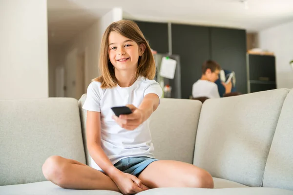 Una chica sosteniendo el control remoto y viendo el programa de televisión — Foto de Stock