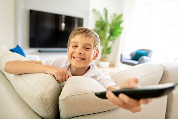 Um menino segurando controle remoto e assistindo programa de TV — Fotografia de Stock