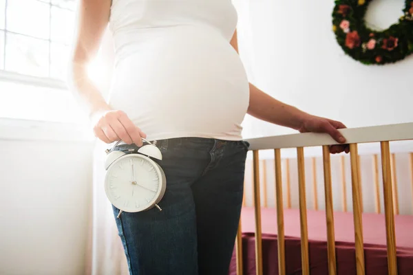 Беременная женщина с часами дома — стоковое фото