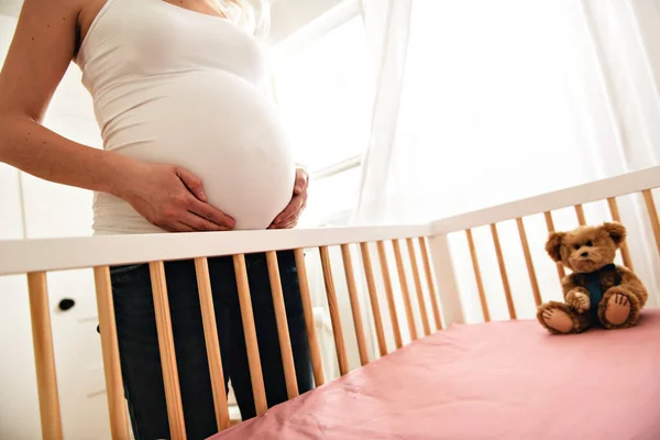Vista en el vientre de la mujer embarazada cerca de la cuna —  Fotos de Stock