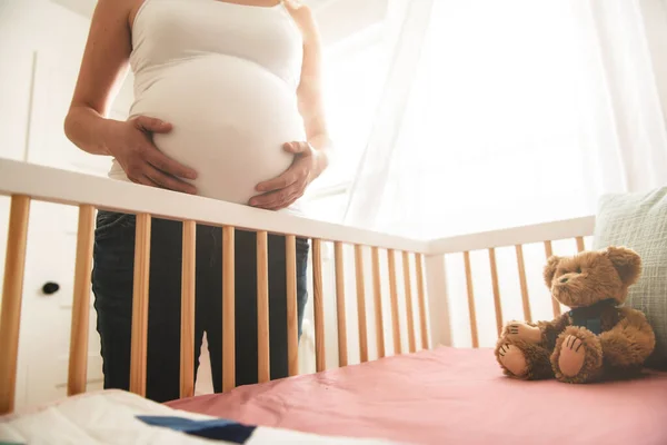 Uitzicht op zwangere vrouw buik dicht bij baby wieg — Stockfoto