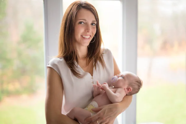 Lycklig familj mamma med nyfött barn framför fönstret — Stockfoto