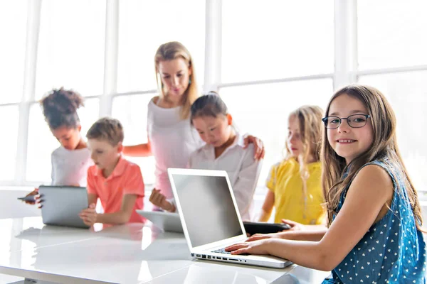 Niño con tecnología tableta y computadora portátil en el aula maestro en el fondo —  Fotos de Stock