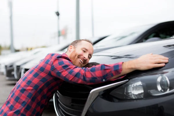 Ein glücklicher junger Mann umarmt sein Auto vor einem Garagenladen — Stockfoto