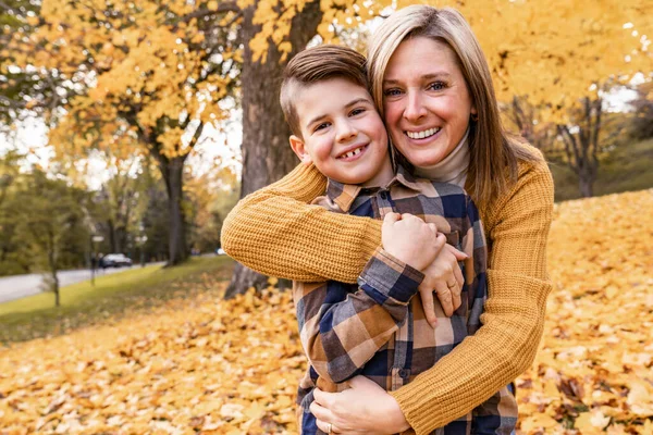 Lycklig familj mor och barn pojke i höst löv falla i parken — Stockfoto