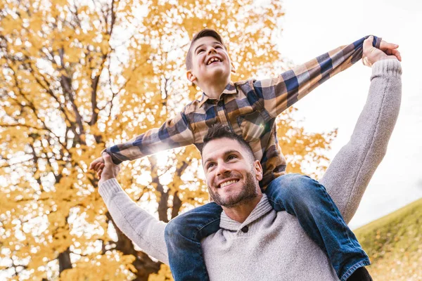 Lycklig familj far och barn pojke på axeln i höst löv falla i parken — Stockfoto