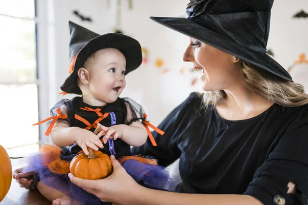 カボチャとハロウィンの準備ができてキッチンテーブルの上の家族の母親と赤ちゃんの娘 — ストック写真