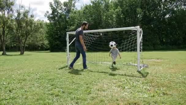 Jovem pai com seu filhinho jogando futebol em campo de futebol — Vídeo de Stock
