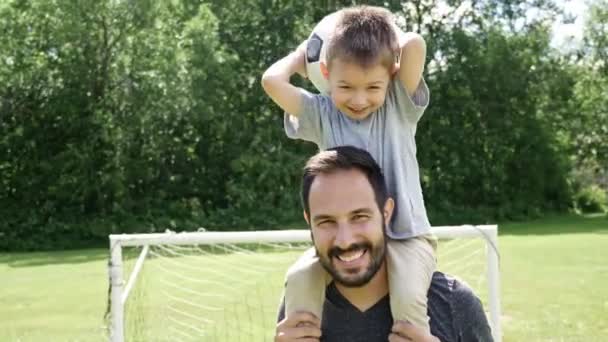 Młody ojciec z synkiem grający w piłkę nożną na boisku — Wideo stockowe