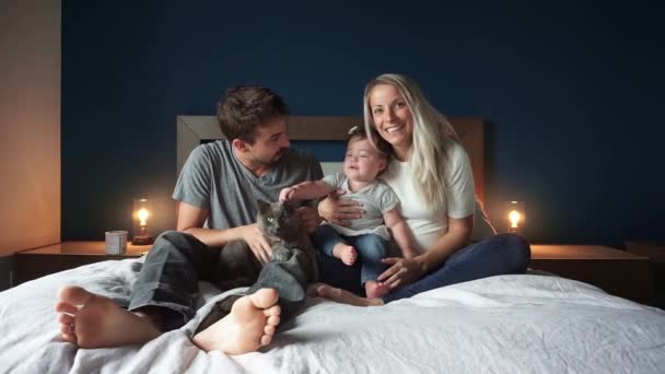 Familie van drie zitten op het bed met 1 jaar kind meisje en kat — Stockvideo