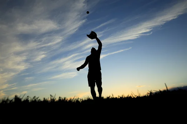 Um homem silhueta pelo pôr do sol está apenas começando a pegar bola com luva — Fotografia de Stock