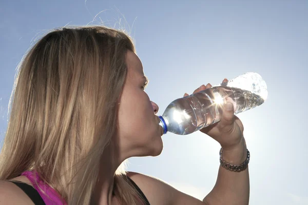 A woman drinking water outside with sky on the background. — Stock Photo, Image