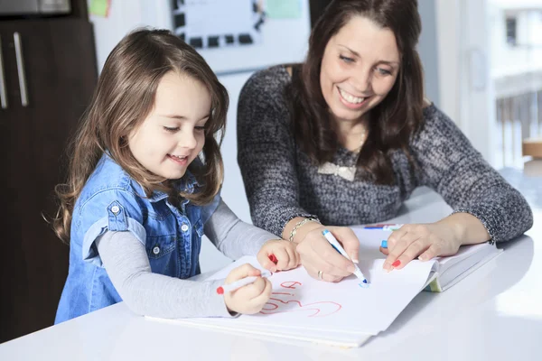 A mother and daughter drawing in a book on the kitchen — Stock Photo, Image