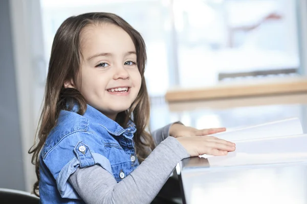 Carina bambina con libro a casa e sorridente — Foto Stock