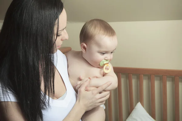 Devoted mother laying son down into crib for nap in bedroom — Stock Photo, Image