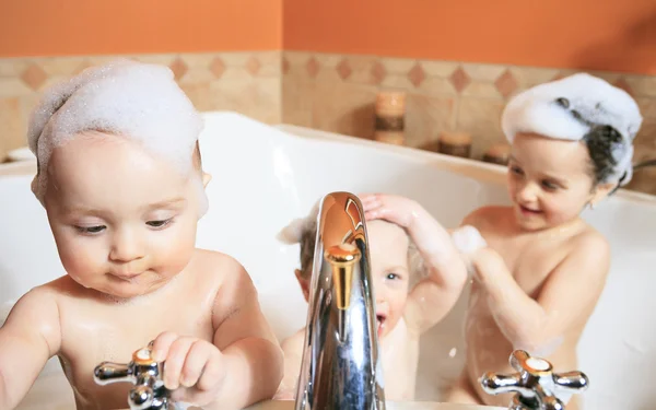 Funny little girl and her cute baby brother having fun taking bath together playing in water with foam with colorful toys after shower