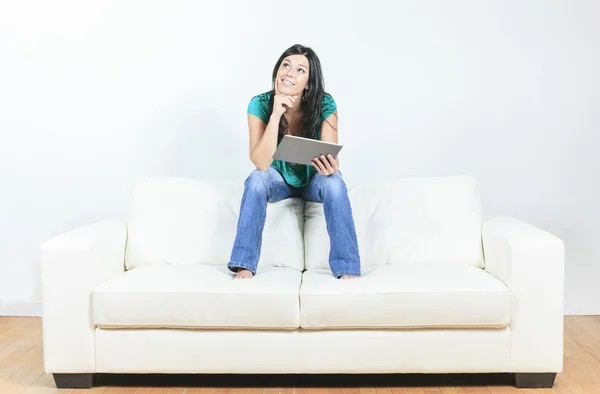 Ung kvinna med elektroniska tablett sitter på soffan — Stockfoto