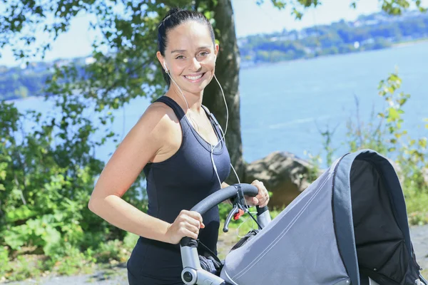 A Young mother jogging with a baby buggy — Stock Photo, Image
