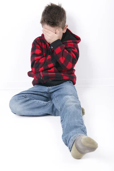 Ein trauriger kleiner Junge sitzt auf weißem Hintergrund — Stockfoto