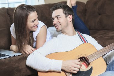 A Handsome man serenading his girlfriend with guitar at home in clipart
