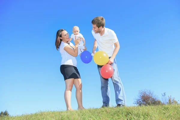 Una familia joven y feliz con un pequeño bebé al aire libre — Foto de Stock