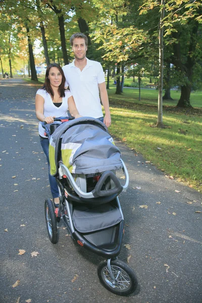 Un couple souriant avec poussette bébé dans un parc — Photo