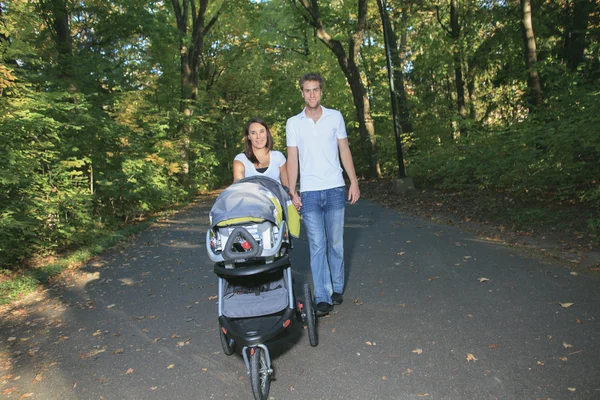 Um casal sorridente com carrinho de bebê em um parque — Fotografia de Stock