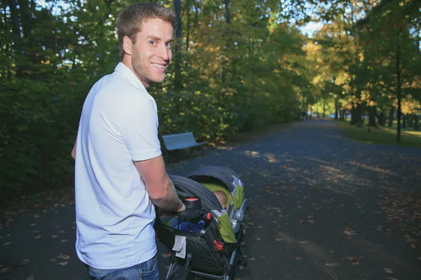 En 30 år gammal man med en barnvagn promenader i parken — Stockfoto