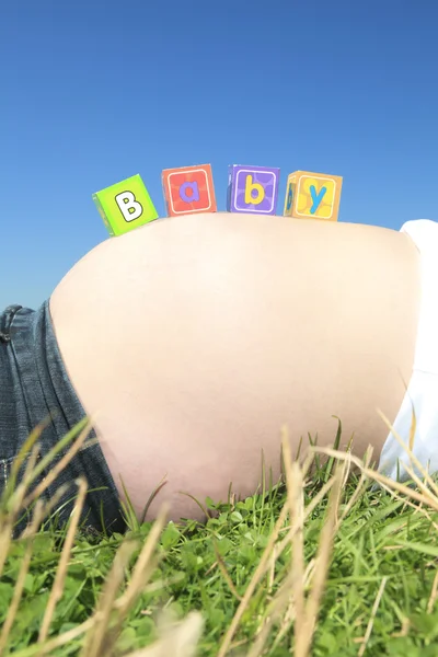 Алфавит блокирует написание "BABY" на беременном животе — стоковое фото
