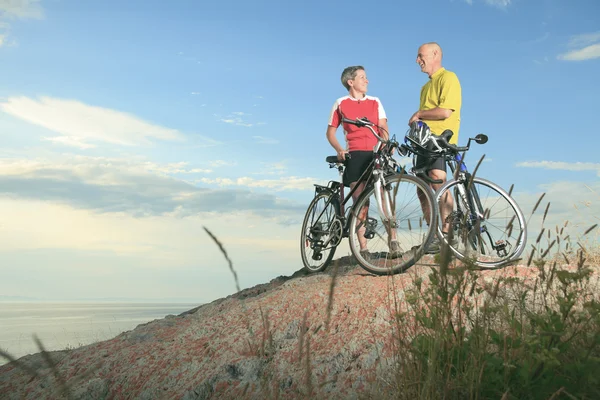 A senior man and a woman on bike at the sunset. — Stock Photo, Image