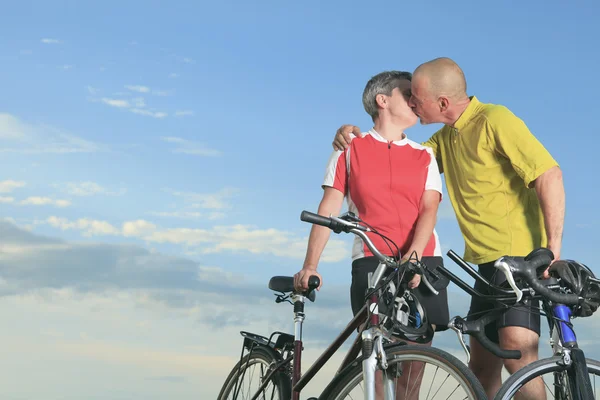 A senior man and a woman on bike at the sunset. — Stock Photo, Image