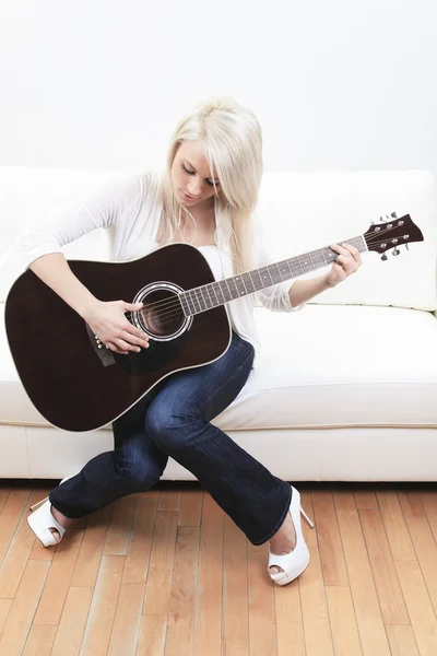 Gyönyörű fiatal nő, a kanapén egy gitár — Stock Fotó
