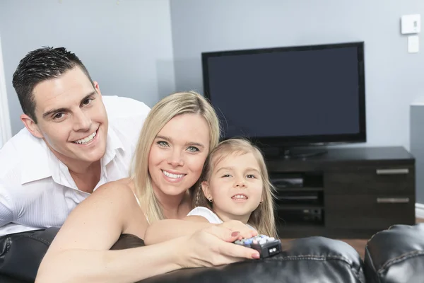 Uma família jovem assistindo TV juntos em casa — Fotografia de Stock