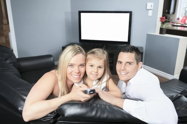 Una familia joven viendo la televisión juntos en casa —  Fotos de Stock