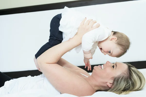 Felice giovane madre che gioca con sua figlia sul letto a casa — Foto Stock