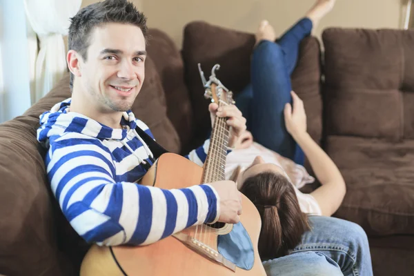 En stilig man serenading sin flickvän med gitarr hemma i — Stockfoto