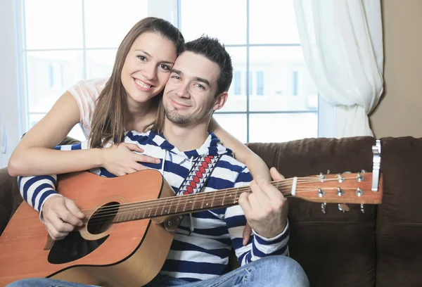 Un bel homme sérénade sa petite amie avec guitare à la maison dans — Photo