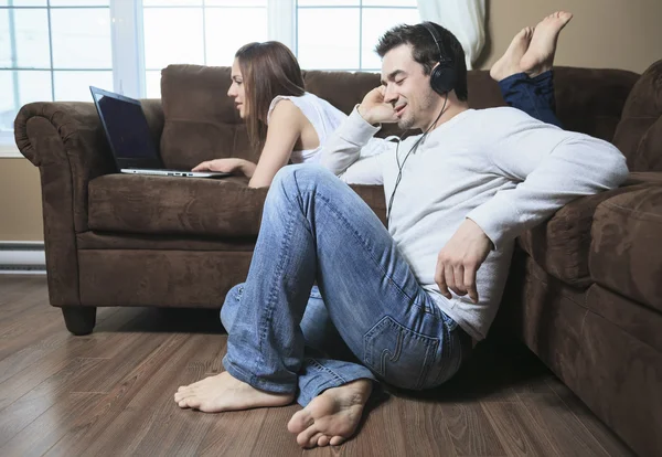 A woman lay on the sofa with laptop and a man ear music — Stock Photo, Image