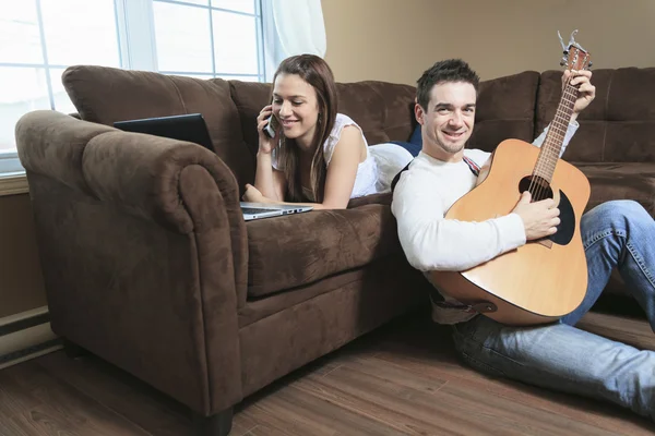 En stilig man serenading sin flickvän med gitarr hemma i — Stockfoto