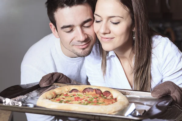 Um jovem casal feliz comendo pizza na cozinha — Fotografia de Stock