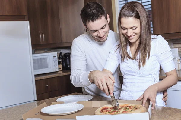 Um jovem casal feliz comendo pizza na cozinha — Fotografia de Stock